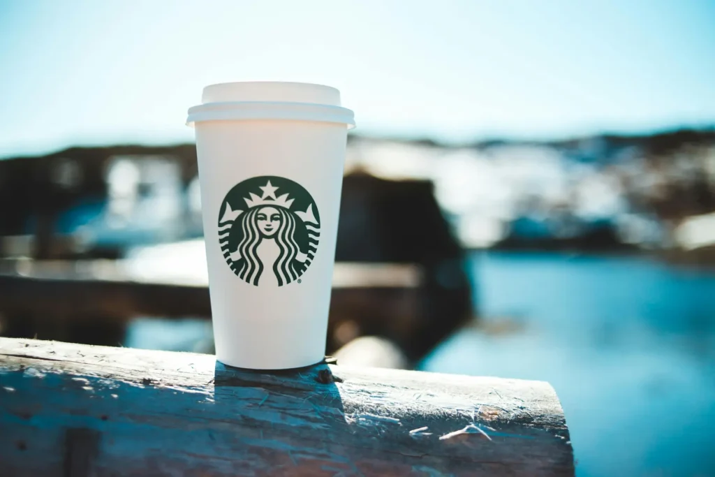 Un gobelet Starbucks posé sur une barrière en bois avec un paysage flou en arrière-plan.